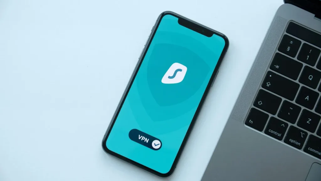 Smartphone menampilkan aplikasi VPN di sebelah laptop di atas meja, menggambarkan keamanan koneksi internet
